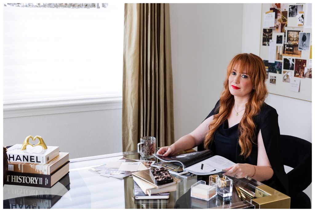 Colorado Springs brand photographer captures luxury brand designer Moriah Riona during her brand photo shoot, seated at a glass desk beneath a crystal chandelier